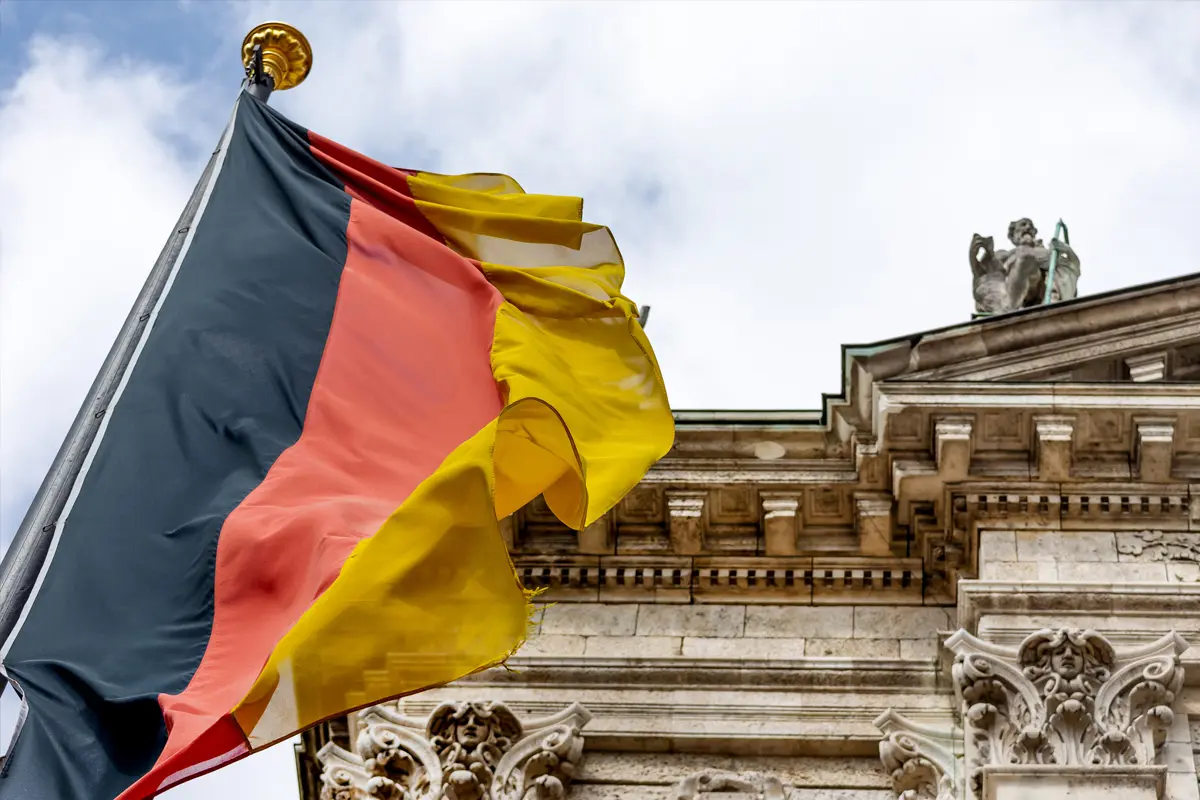 Vor einem klassischen Steingebäude weht die deutsche Flagge am Fahnenmast