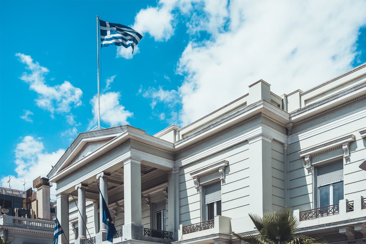 Imposantes Gebäude im klassischen Stil, auf dessen Dach mehrere griechische Flaggen wehen