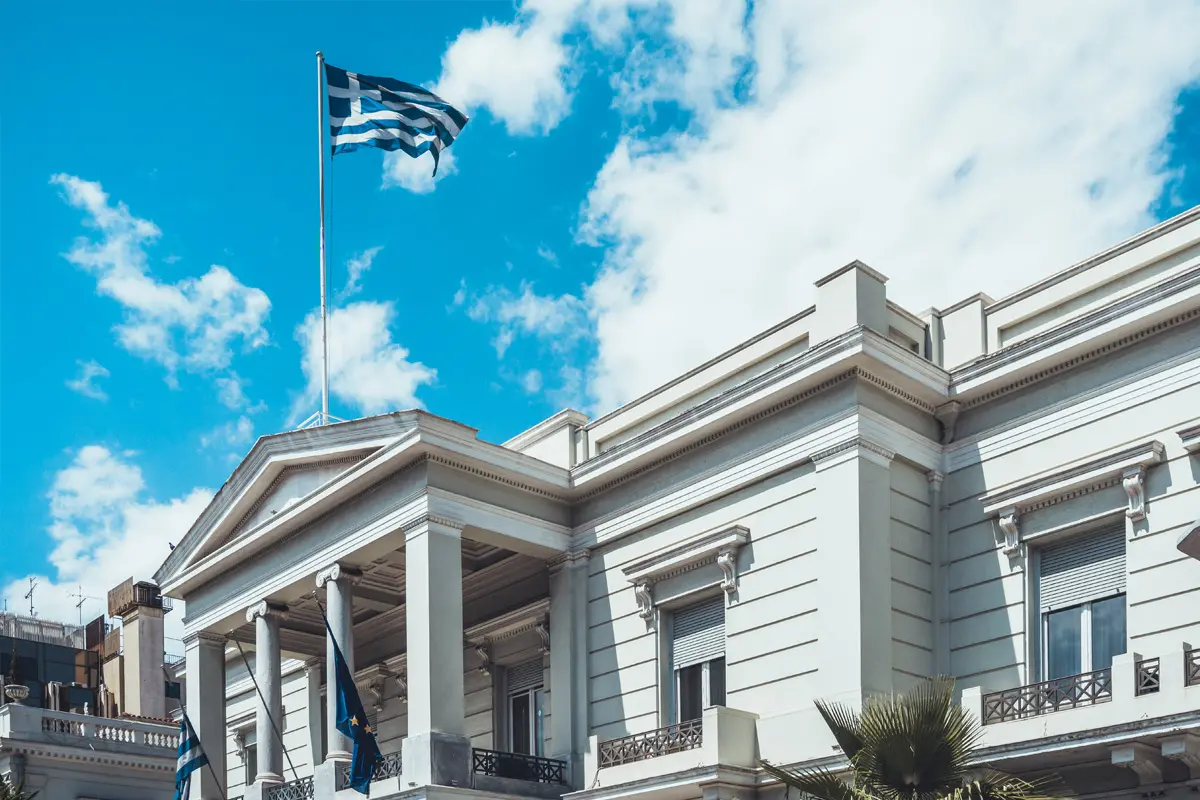 Imposantes Gebäude im klassischen Stil, auf dessen Dach mehrere griechische Flaggen wehen